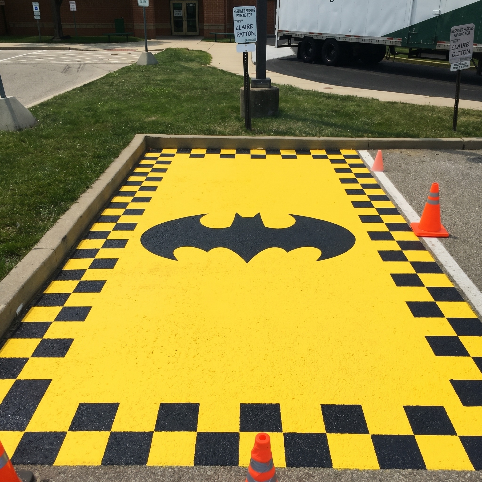 Show a parking spot with a bat symbol in the center and a checkered black and yellow border around the edges, shot from overhead to show the full frame and center design. Colors should be bold black and yellow, playful and energetic mood.